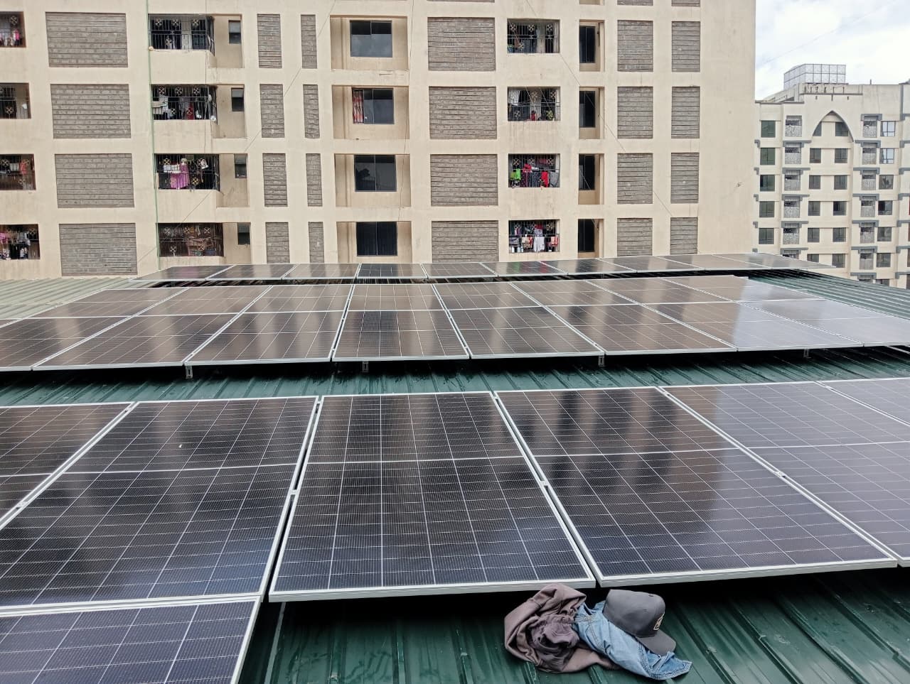 Tilted solar panel mounting rails installed on a green metal roof of a residential apartment block